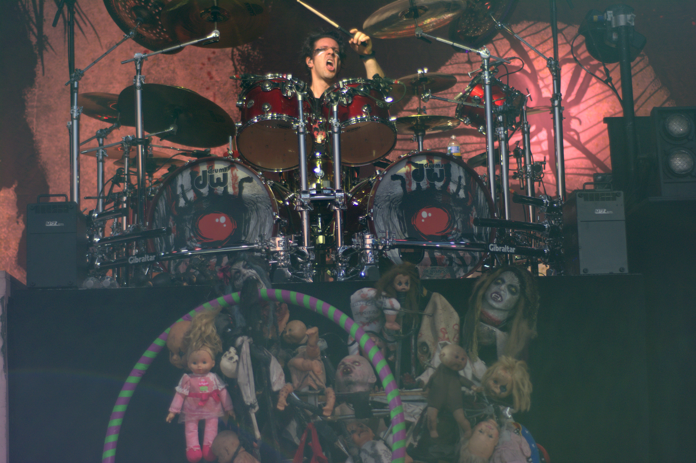 A drummer performs behind a large kit and theatrical stage props.