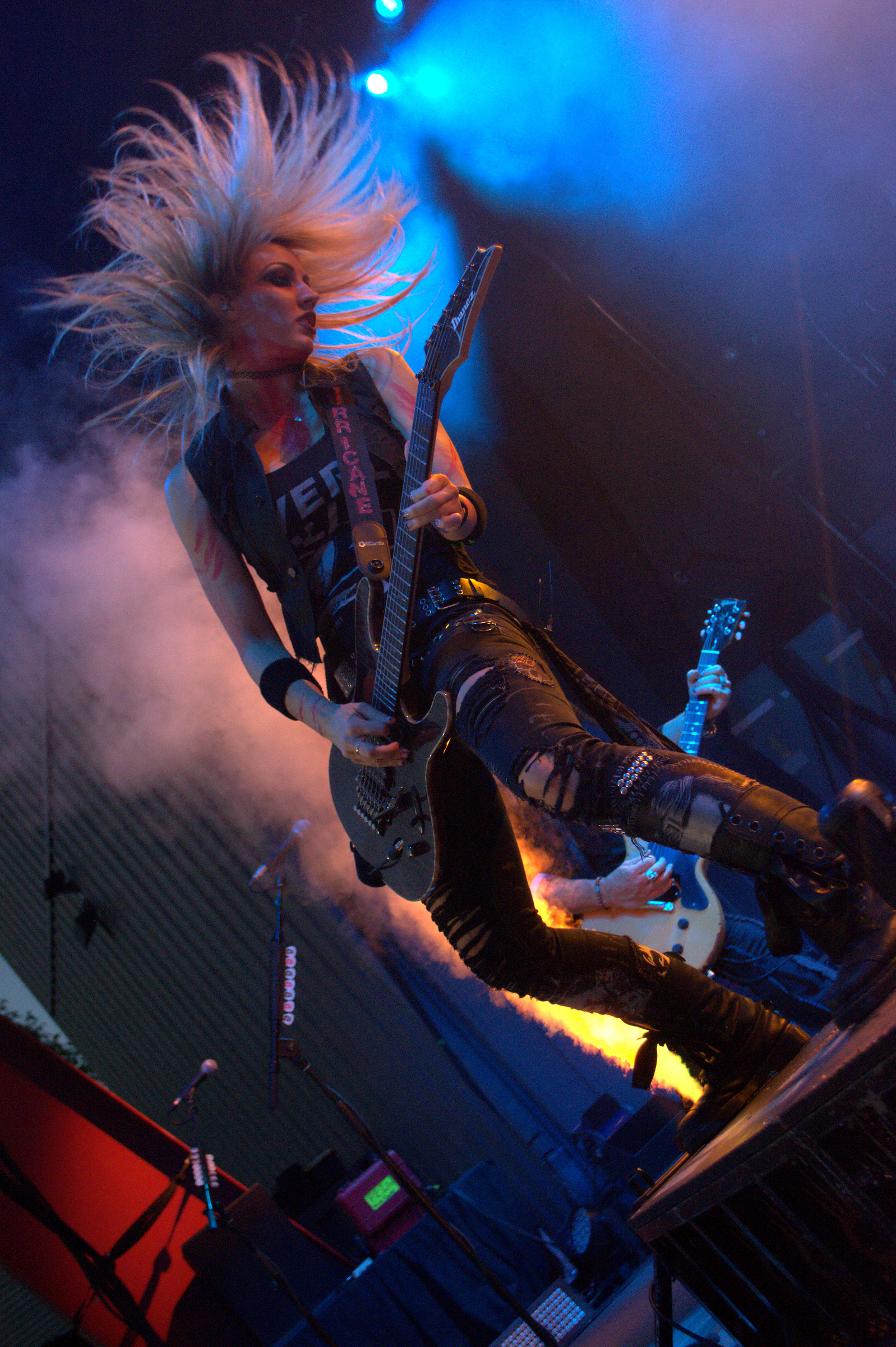 A guitarist performs with flying hair beneath blue and orange stage lights.